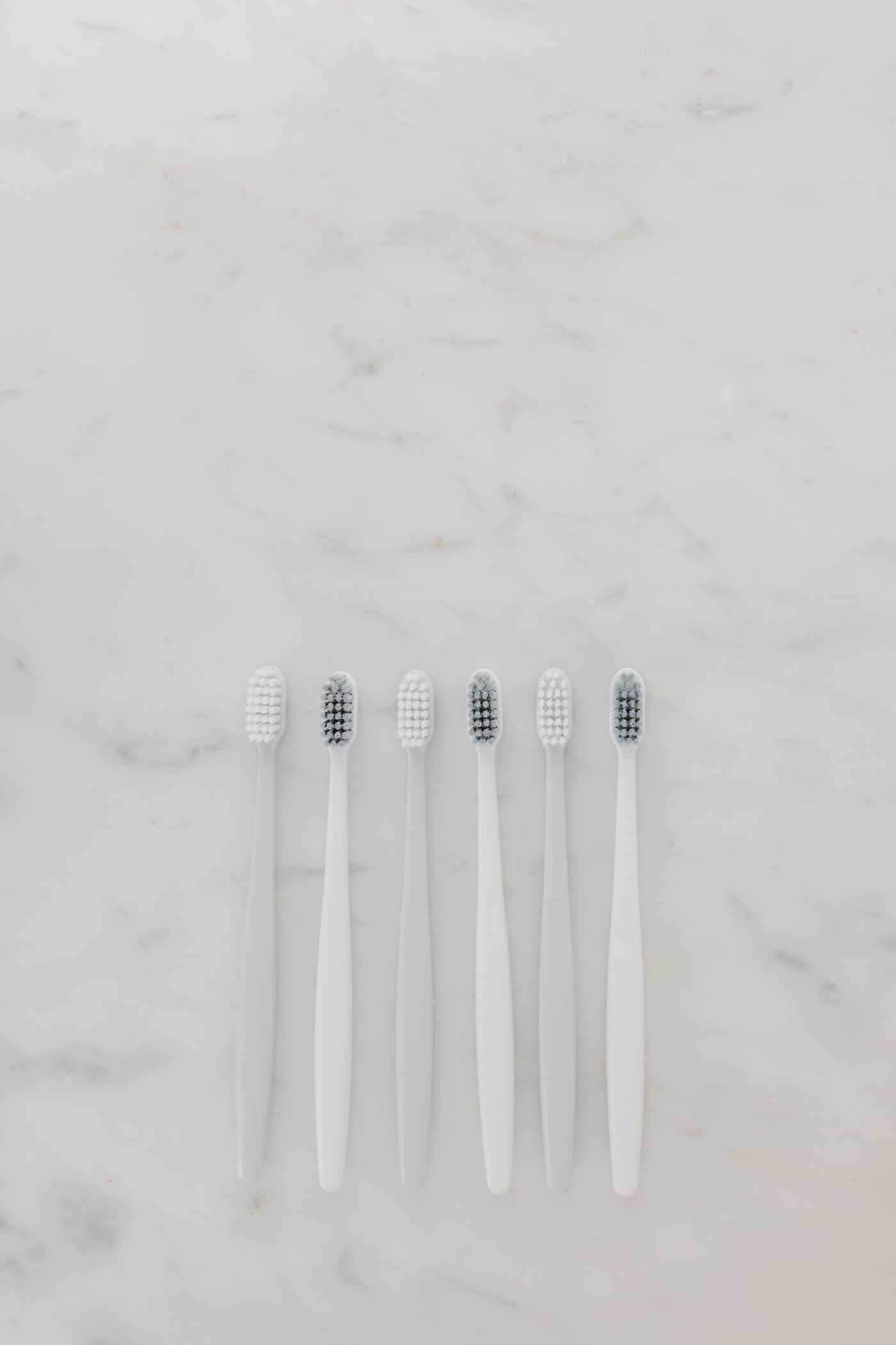 Six white toothbrushes lined up on a marble surface